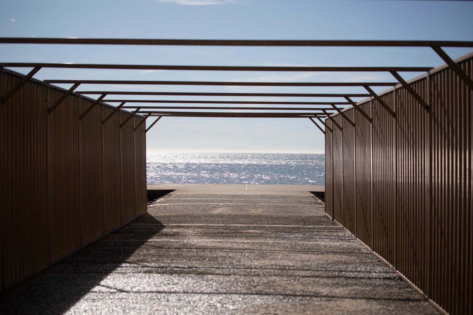 Un passage de bois vers la mer, la lumière tombant en lames entre les planches